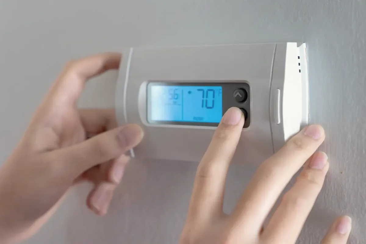 Hands adjusting a digital wall thermostat